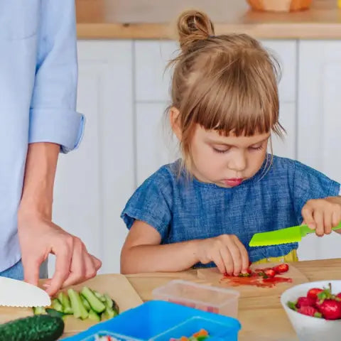 Jong kind snijdt groenten met kindvriendelijke messen op houten snijplank.