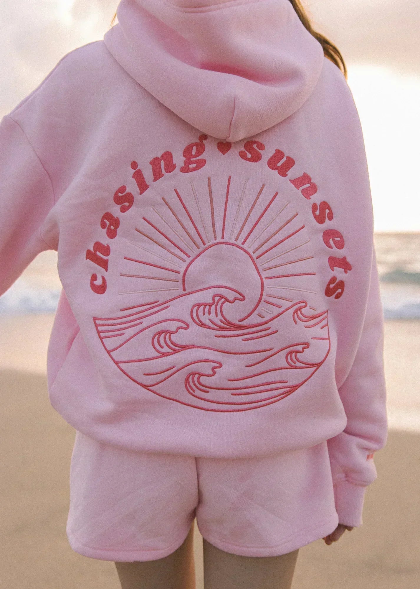 Roze sweatshirt met chasing sunsets tekst en zon-en-golven graphic voor ultiem comfort.